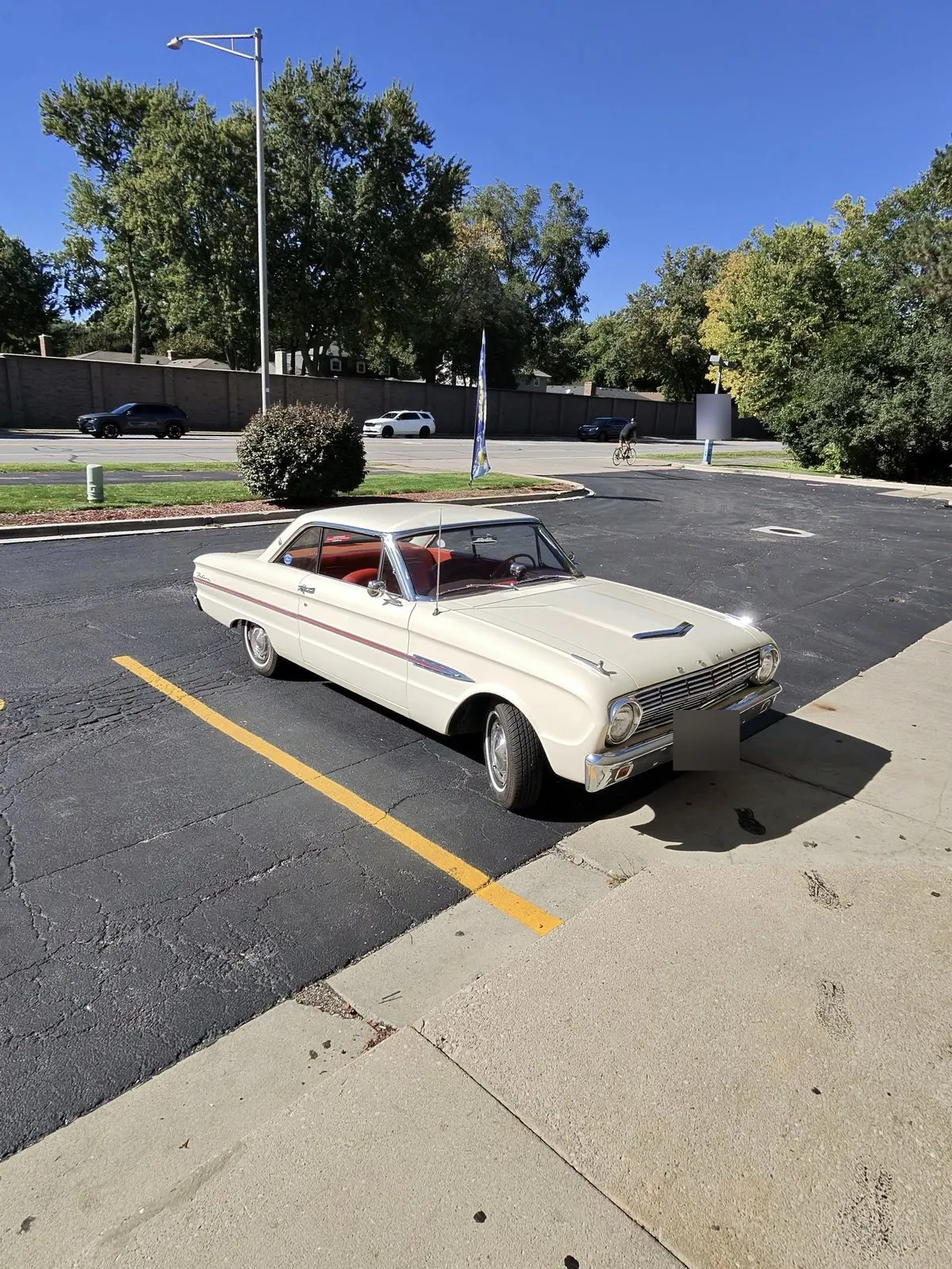 A cream 1963 Ford Falcon hardtop parked in a sunny parking lot, with the license plate blurred