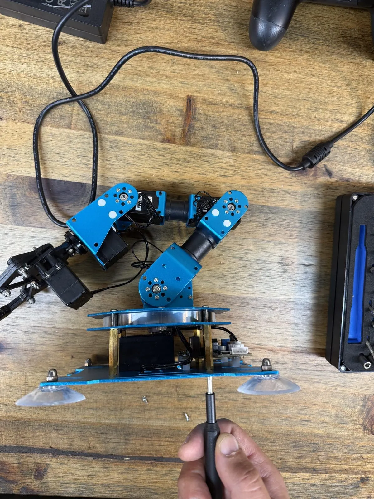 Hiwonder xArm on a workbench with a screwdriver removing the base plate to reach the stock controller board