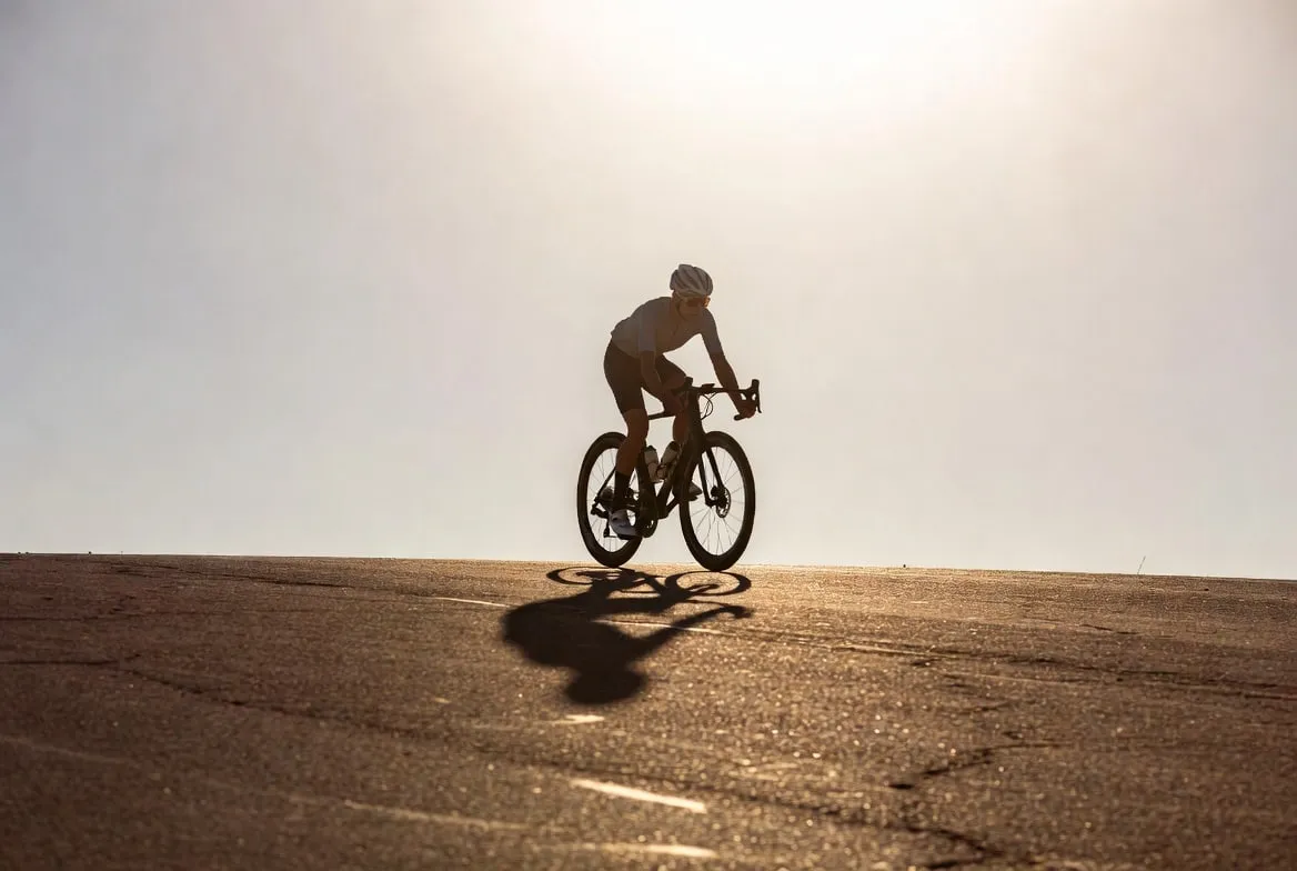A lone cyclist cresting a warm, sunlit hill on an open road, with the sky as wide negative space