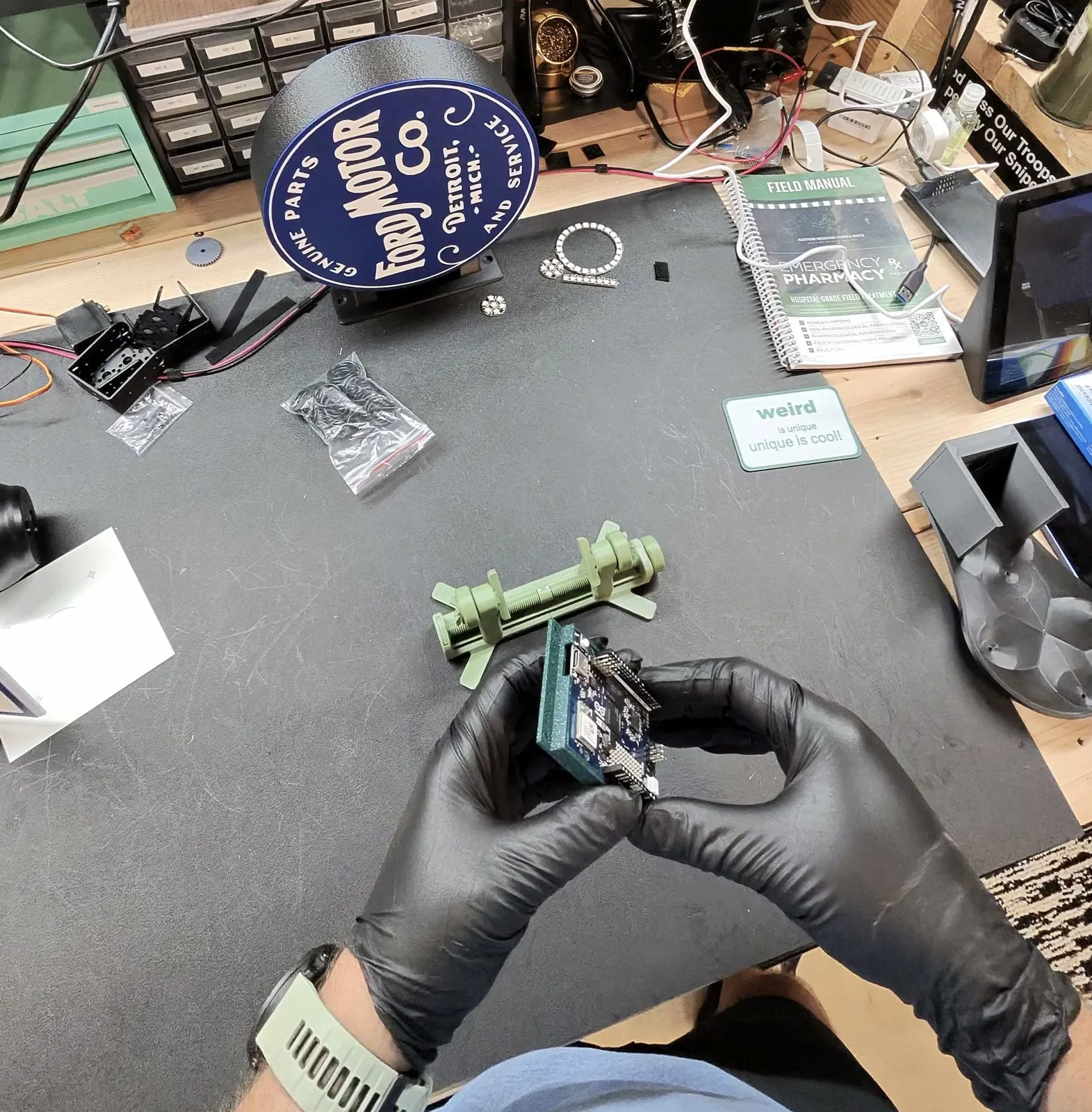 Gloved hands holding an Arduino Uno Q seated in a freshly printed green case on a workbench